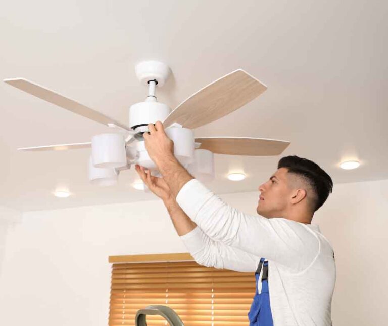 A man repairs a ceiling fan in a home, using tools and standing on a ladder for better access